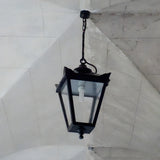 Medium Victorian cast iron hanging lantern in black, tapered four-sided glass head with stepped crown and finial, suspended by chain from a stone vaulted ceiling.