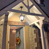Small Victorian cast iron hanging lantern in black, four-sided glass head on a chain, illuminated beneath a porch gable at a covered entrance.