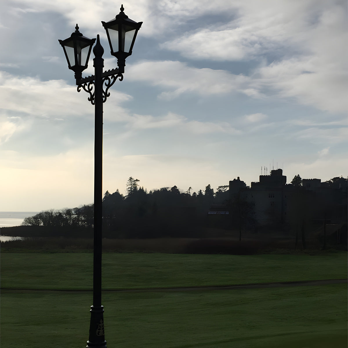 Victorian cast iron double-headed lamp post, 3.3m tall in black, with tapered four-sided lantern heads and scrollwork bracket, shown outdoors on a lawn against a cloudy sky.