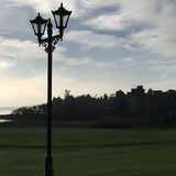 Victorian cast iron double-headed lamp post, 3.3m tall in black, with tapered four-sided lantern heads and scrollwork bracket, shown outdoors on a lawn against a cloudy sky.