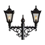 Victorian cast iron double-headed lamp post in black, featuring two tapered lantern heads with glass panels, illuminated bulbs, scrolled brackets, and a central finial on a plain white background.