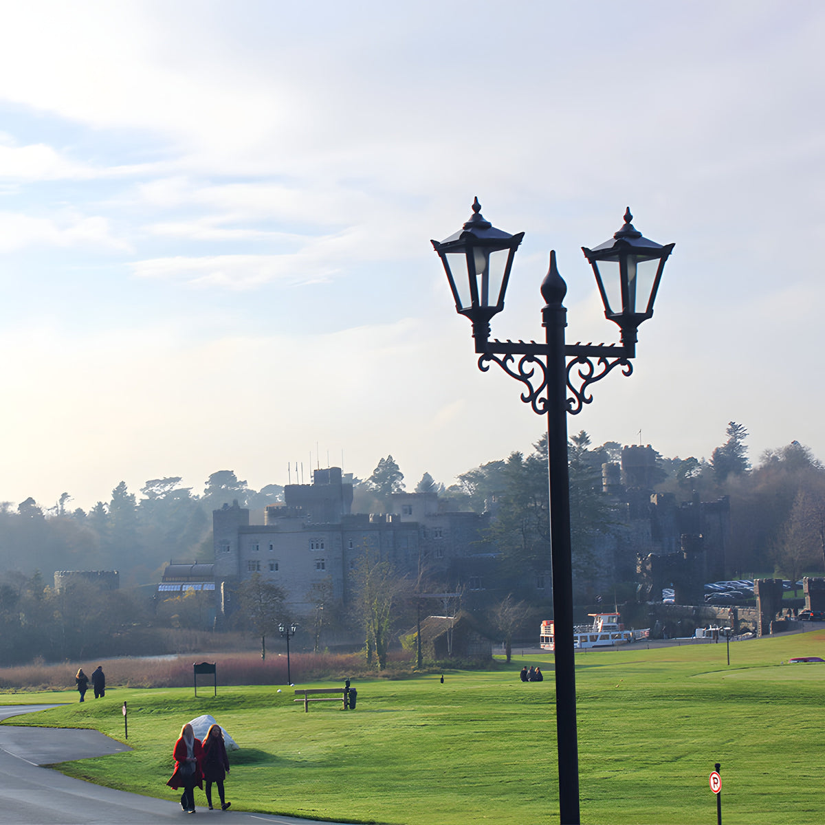 Victorian cast iron double-headed lamp post in black, 3.3m tall with two traditional lantern heads on curved brackets, shown outdoors on parkland near a castle.