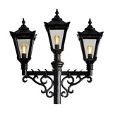Victorian cast iron triple-headed lamp post in black with three tapered lantern heads, scrolled cross arm brackets and glowing bulbs, shown on a plain white background.