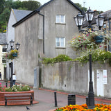 Victorian cast iron triple-headed lamp post in black, tapered lantern heads with stepped crowns, shown outdoors on a paved street lined with hanging flower baskets.