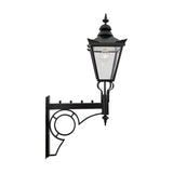 Large Victorian wall lantern in black with a tapered four-sided glass head, stepped crown, cast finial, and E27 bulb, mounted on an ornate scroll bracket against a plain white background.