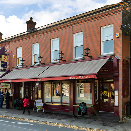 Victorian cast iron wall lanterns on long black arms mounted in a row along a red brick building facade, tapered four-sided heads with stepped crowns.