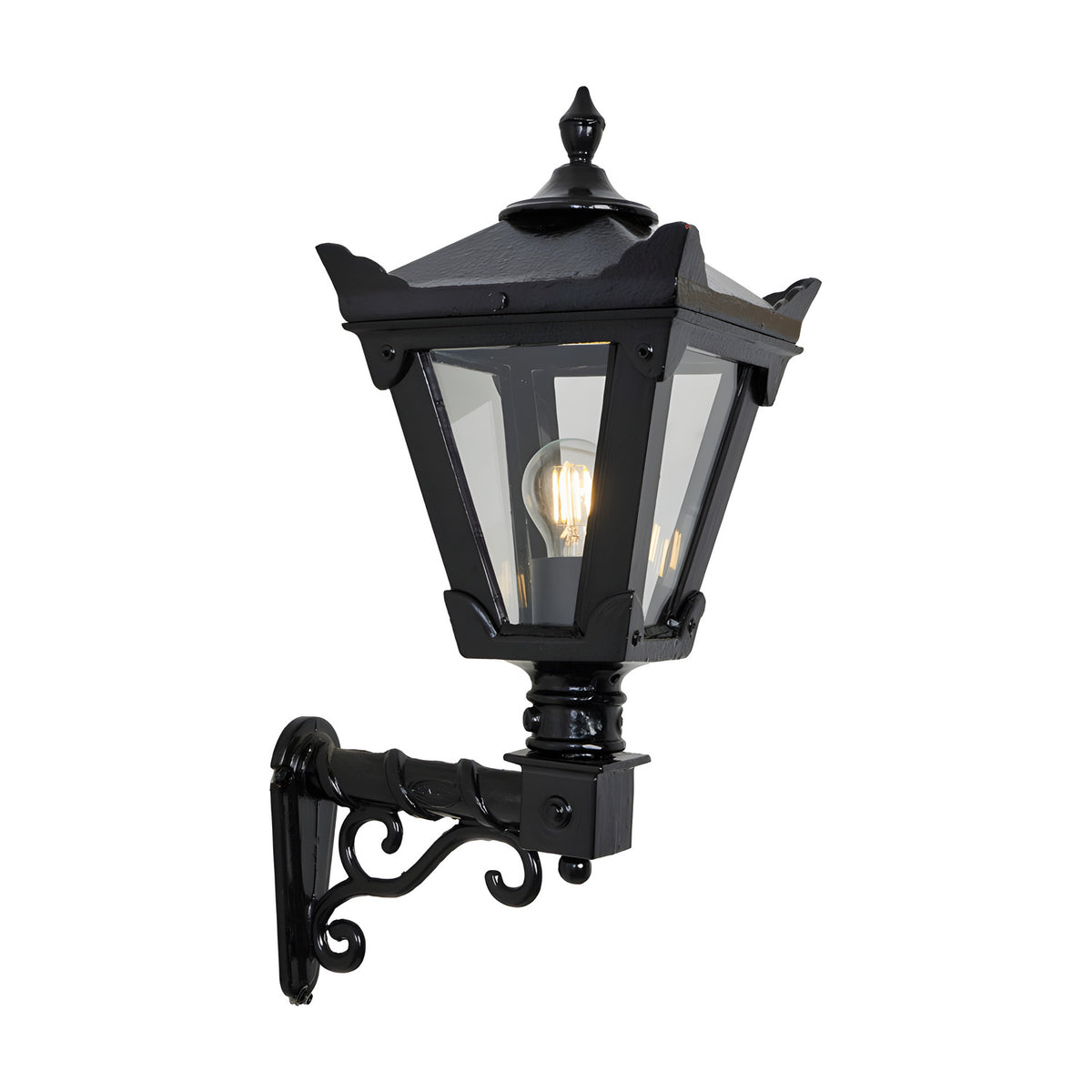 Small Victorian wall lantern in black with tapered four-sided glass head, stepped crown finial, and cast scroll bracket, shown lit on a plain white background.