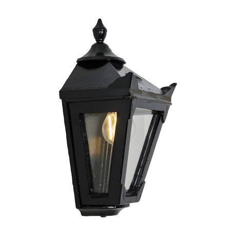 Small Victorian Cast Iron Half Lantern Wall Light in black, tapered four-sided glass head with stepped crown and cast finial, lit bulb visible, plain white background.