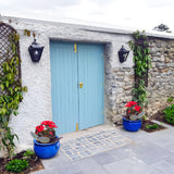 Small Victorian half lantern wall lights in black cast iron with glass panels, mounted either side of a pale blue door on a white stone wall.