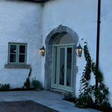 Large Victorian Cast Iron Half Lantern Wall Light in black, mounted either side of an arched front door on a white rendered house facade at dusk.