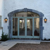 Large Victorian half lantern wall lights in black cast iron with glass panels, mounted either side of an arched glazed doorway on a white rendered exterior.
