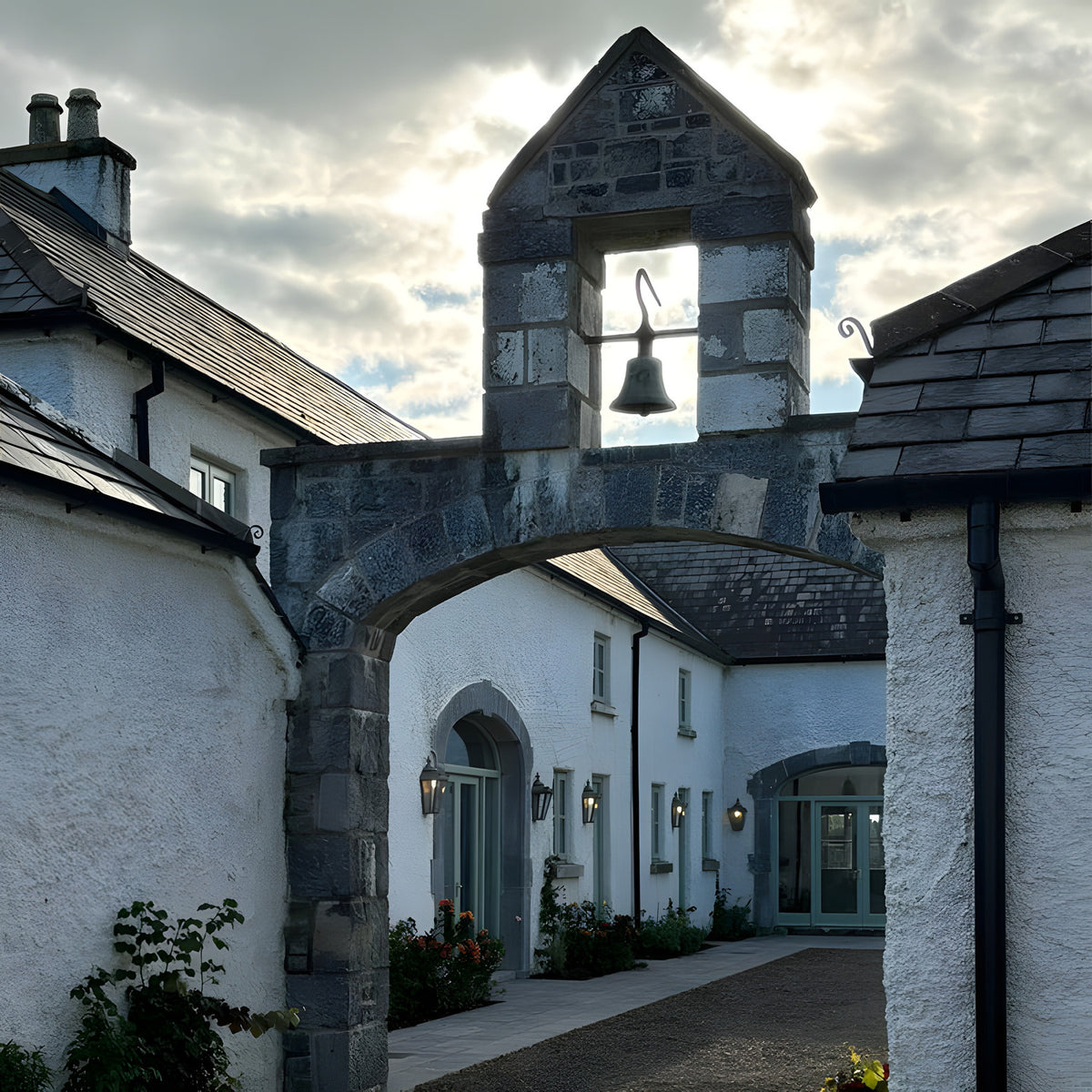 Large Victorian half lantern wall light in black cast iron with glass panels, mounted beneath an archway bell tower at a stone building entrance.