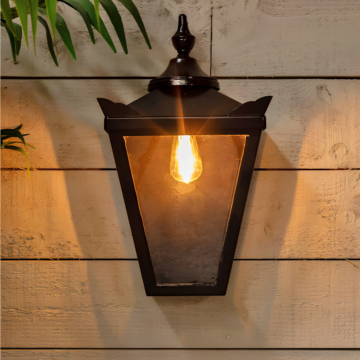 Large Victorian half lantern wall light in black cast iron with clear glass panels, mounted on a wooden wall, lit with a warm E27 bulb.