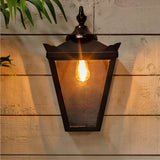 Large Victorian half lantern wall light in black cast iron with clear glass panels, mounted on a wooden wall, lit with a warm E27 bulb.
