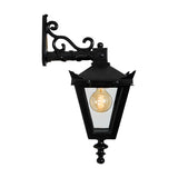 Victorian cast iron downturned wall lantern in black with a scrolled bracket and tapered glass-panelled head, shown lit with a bulb on a plain white background.