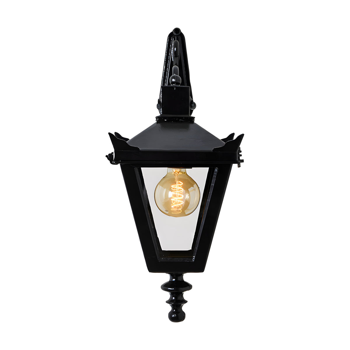 Victorian downturned wall lantern in black cast iron with a tapered four-sided glass head, stepped crown, corner tips and cast finial, shown lit on a plain white background.