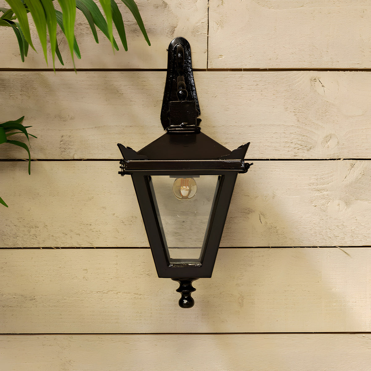 Victorian Cast Iron Downturned Wall Lantern in black, tapered four-sided glass head with stepped crown and cast finial, mounted on a wooden panelled wall.