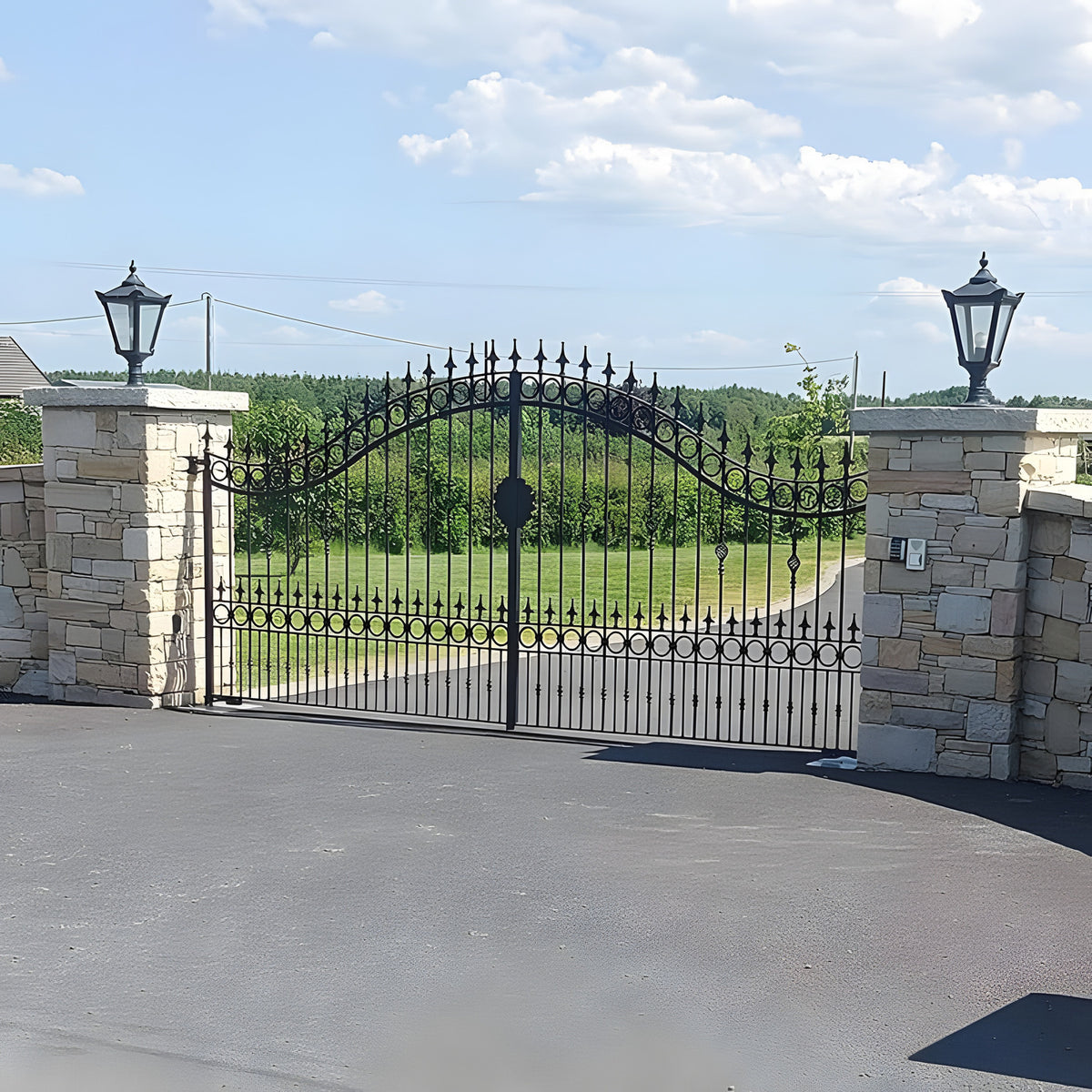 Black Victorian cast iron pillar light with tapered four-sided head and stepped crown, mounted on a stone gate pier beside an ornate iron gate.