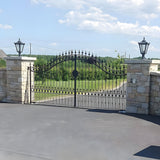 Black Victorian cast iron pillar light with tapered four-sided head and stepped crown, mounted on a stone gate pier beside an ornate iron gate.