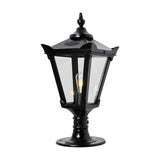 Black cast iron Victorian pillar light with tapered four-sided lantern, clear glass panels, stepped crown, corner tips, cast finial, and pier cap base, shown lit on a white background.