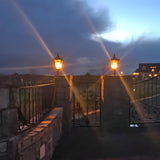 Medium Victorian cast iron pillar lights in black, tapered lantern heads with stepped crowns lit atop matching stone gate piers at dusk.