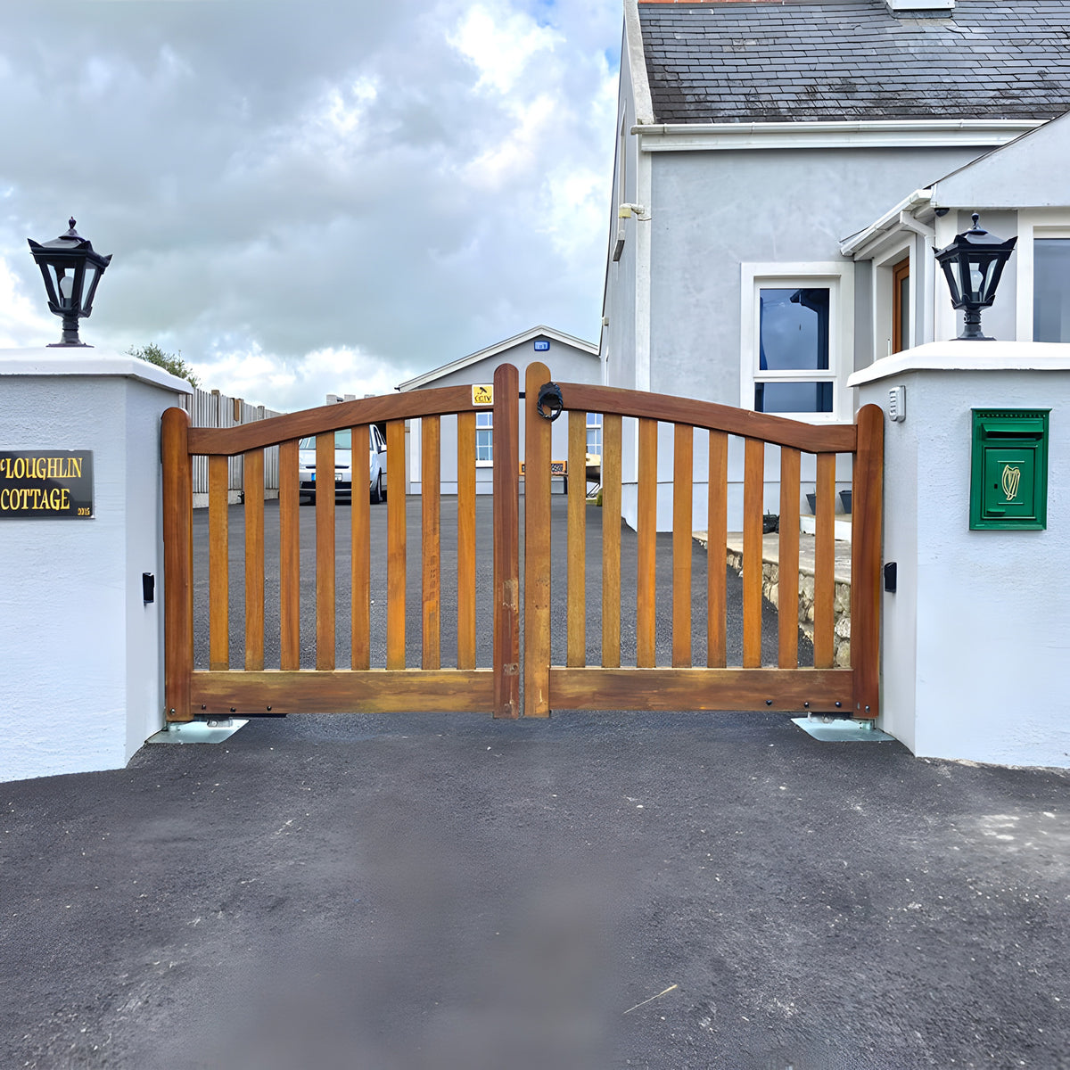 Small Victorian cast iron pillar light in black mounted on a stone gate pier, tapered four-sided lantern head with stepped crown and finial, flanking a wooden driveway gate.