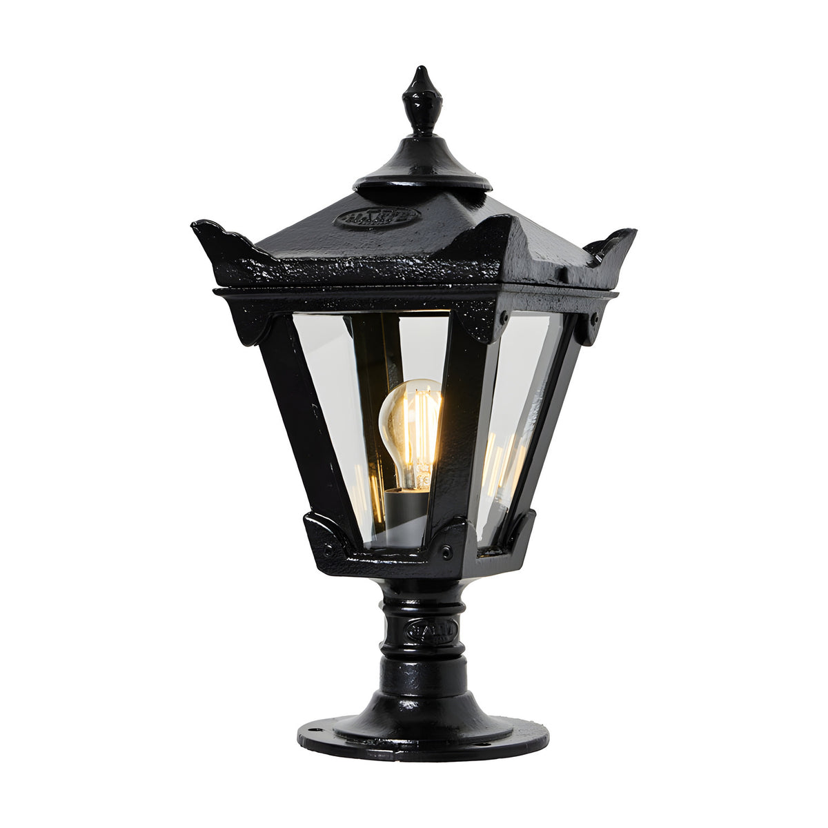 Small Victorian cast iron pillar light in black, tapered four-sided glass head with stepped crown and finial, mounted on pedestal base, lit bulb visible, plain white background.