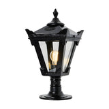 Small Victorian cast iron pillar light in black, tapered four-sided glass head with stepped crown and finial, mounted on pedestal base, lit bulb visible, plain white background.