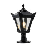 Small Victorian cast iron pillar light in black with a tapered four-sided glass lantern, stepped crown, corner tips and cast finial, shown lit on a pedestal base against a plain white background.