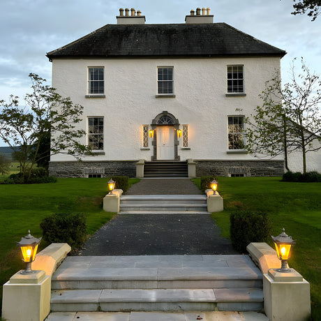 Small Victorian cast iron pillar light in black atop stone pier caps flanking stone steps at a period house entrance, tapered four-sided lantern head with cast finial.