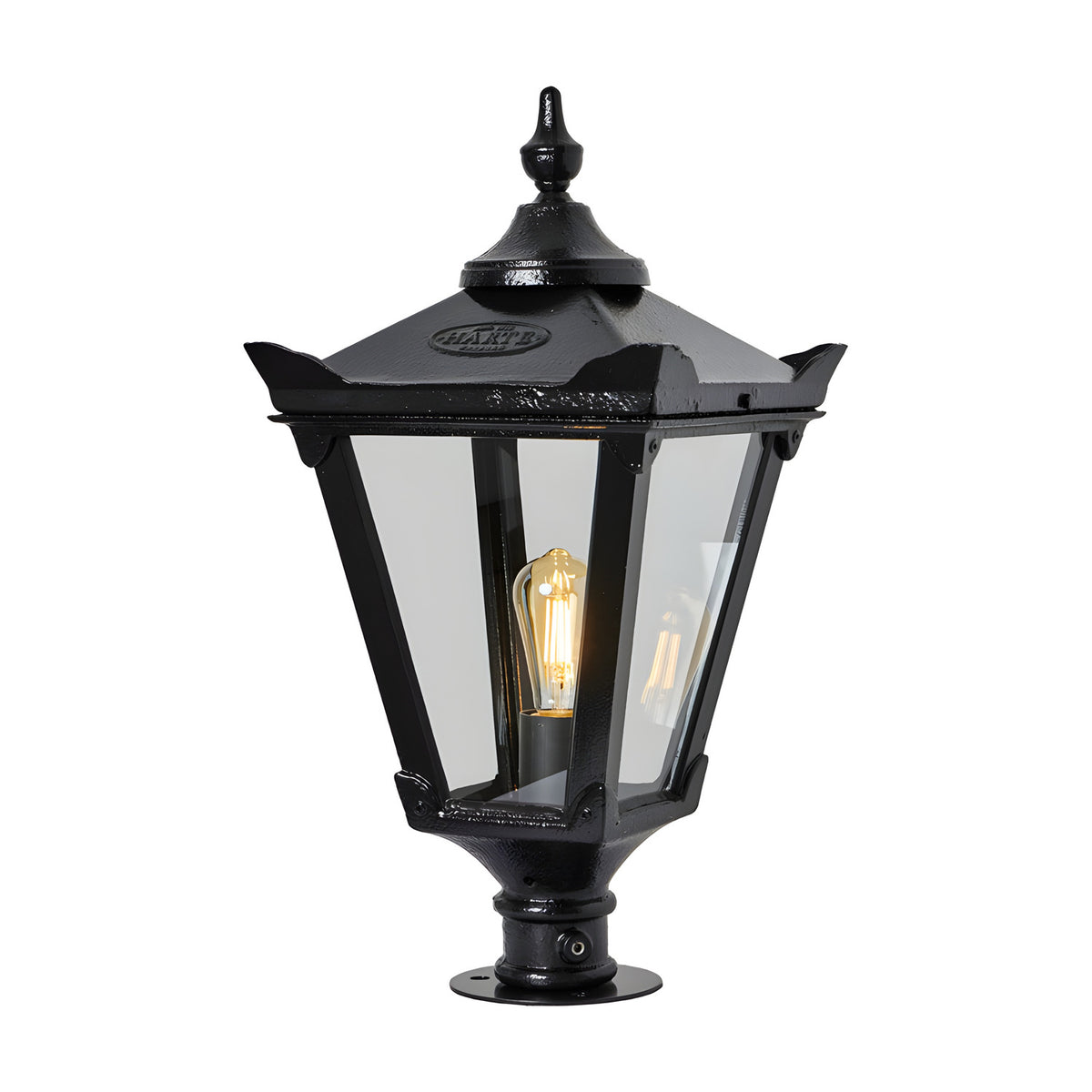 Large Victorian cast iron pillar light in black with a tapered four-sided glass head, stepped crown, corner tips, cast finial, and pier-mount base, shown lit on a plain white background.