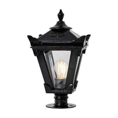 Small Victorian cast iron pillar light in black with tapered four-sided glass head, stepped crown finial and pier-cap base, shown lit against a plain white background.