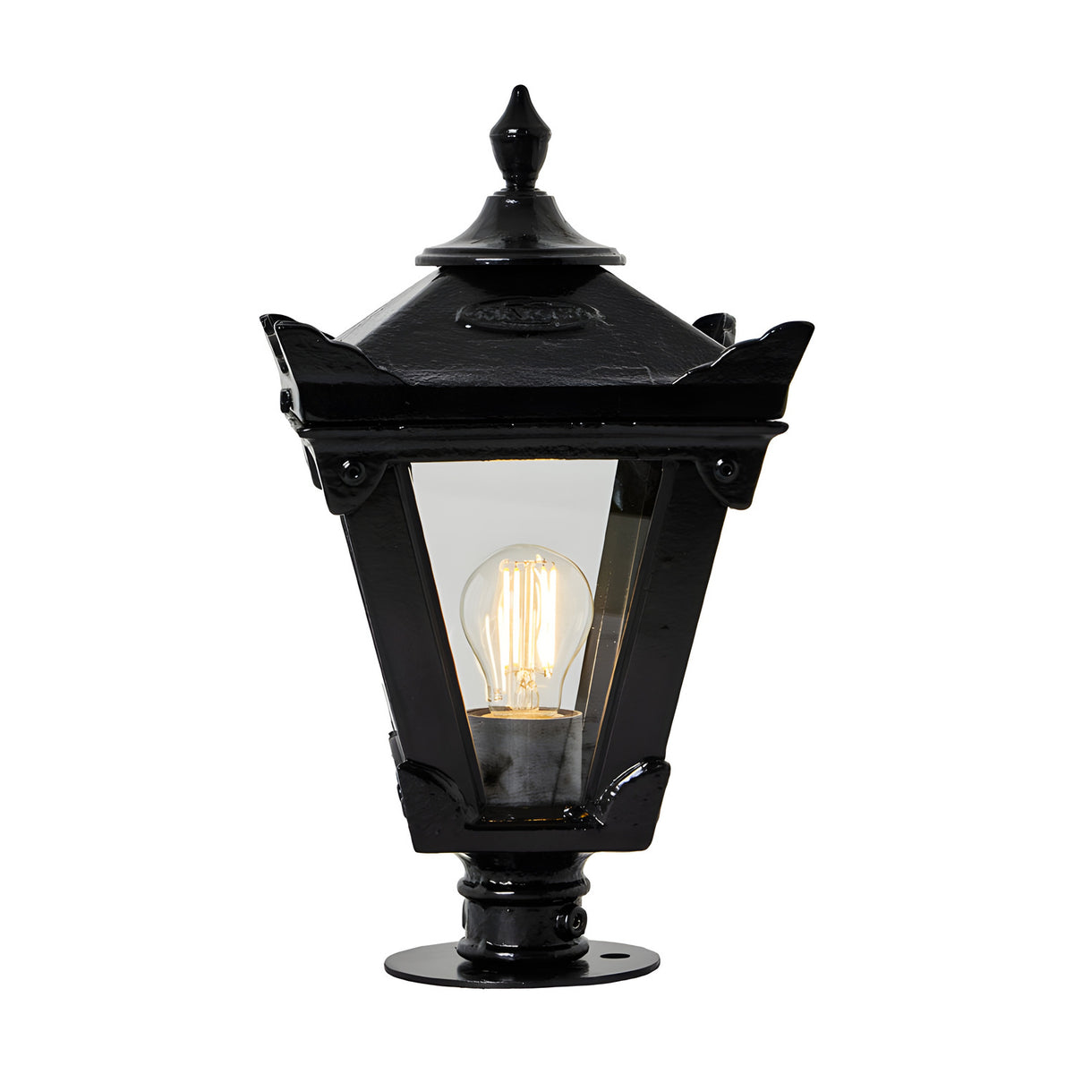 Small Victorian cast iron pillar light in black with tapered four-sided glass panels, stepped crown, corner tips, cast finial and pier cap base, lit bulb visible, on a plain white background.