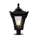 Small Victorian cast iron pillar light in black with tapered four-sided glass panels, stepped crown, corner tips, cast finial and pier cap base, lit bulb visible, on a plain white background.