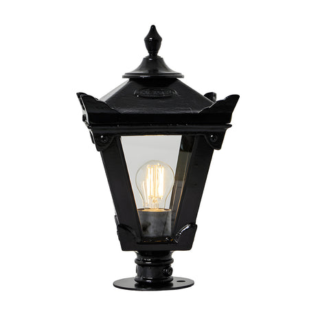Small Victorian cast iron pillar light in black with tapered four-sided glass panels, stepped crown, corner tips, cast finial and pier cap base, lit bulb visible, on a plain white background.