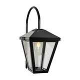Contemporary downturned wall lantern in black metal with clear glass panels and a curved top bracket, shown lit with a visible bulb on a plain white background.