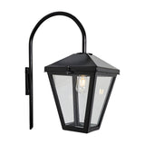 Contemporary downturned wall lantern in black steel with a tapered glass panel shade and curved gooseneck arm on a wall mount, shown lit with an E27 bulb against a plain white background.