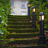 Extra Large Victorian Cast Iron Bollard Light in black, three lit along mossy stone steps with a domed cap and frosted lens, set in a garden path.