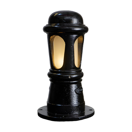 Small Victorian cast iron bollard light in black, domed top, arched frosted lens panels, beaded column on a round base plate, lit from within, on a plain white background.