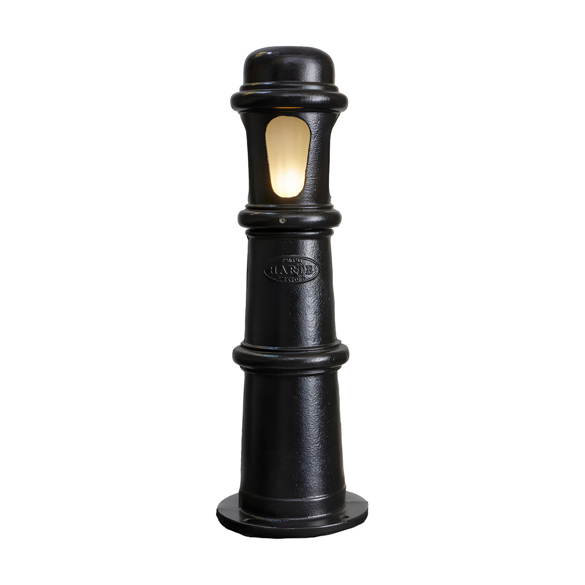 Large Victorian cast iron bollard light in black, a stepped beaded column with a frosted polycarbonate lens window illuminated, on a plain white background.