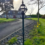 Victorian Cast Iron Globe Lamp Post 1.4m in black, with a caged globe shade on a decorative pole, installed on a gravel border beside a driveway.