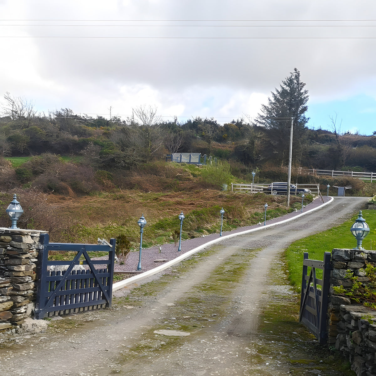 Victorian Cast Iron Globe Lamp Post 1.4m in black, shown lining a gravel driveway alongside matching lamp posts leading to a countryside gate entrance.