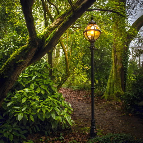 Victorian Cast Iron Globe Lamp Post 2.7m in black, single globe head in banded cage with lit E27 bulb, tall traditional post set on a garden path amid trees.