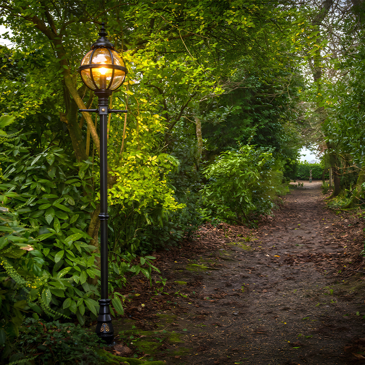 Victorian Cast Iron Globe Lamp Post in black, 2.7m tall with a lit spherical caged shade, set along a leafy garden path.