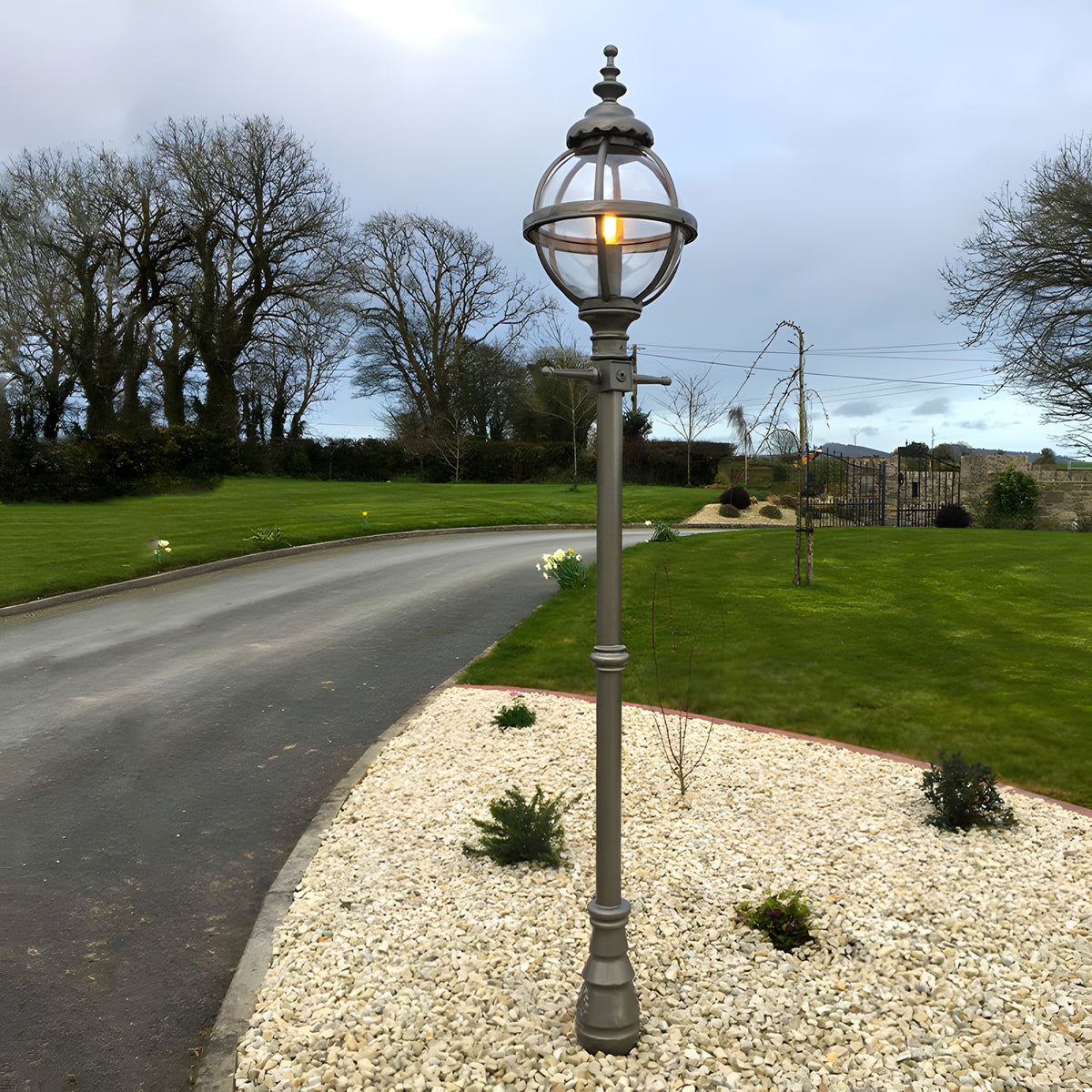 Victorian Cast Iron Globe Lamp Post, 2.5m tall in black, with illuminated glass globe on a banded cage top, set on a gravel bed beside a driveway and lawn.