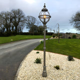 Victorian Cast Iron Globe Lamp Post, 2.5m tall in black, with illuminated glass globe on a banded cage top, set on a gravel bed beside a driveway and lawn.