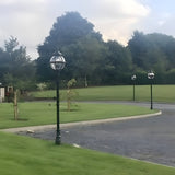 Victorian Cast Iron Globe Lamp Post 2.5m in black, shown on a lawn beside a driveway with matching posts and trees in the background.