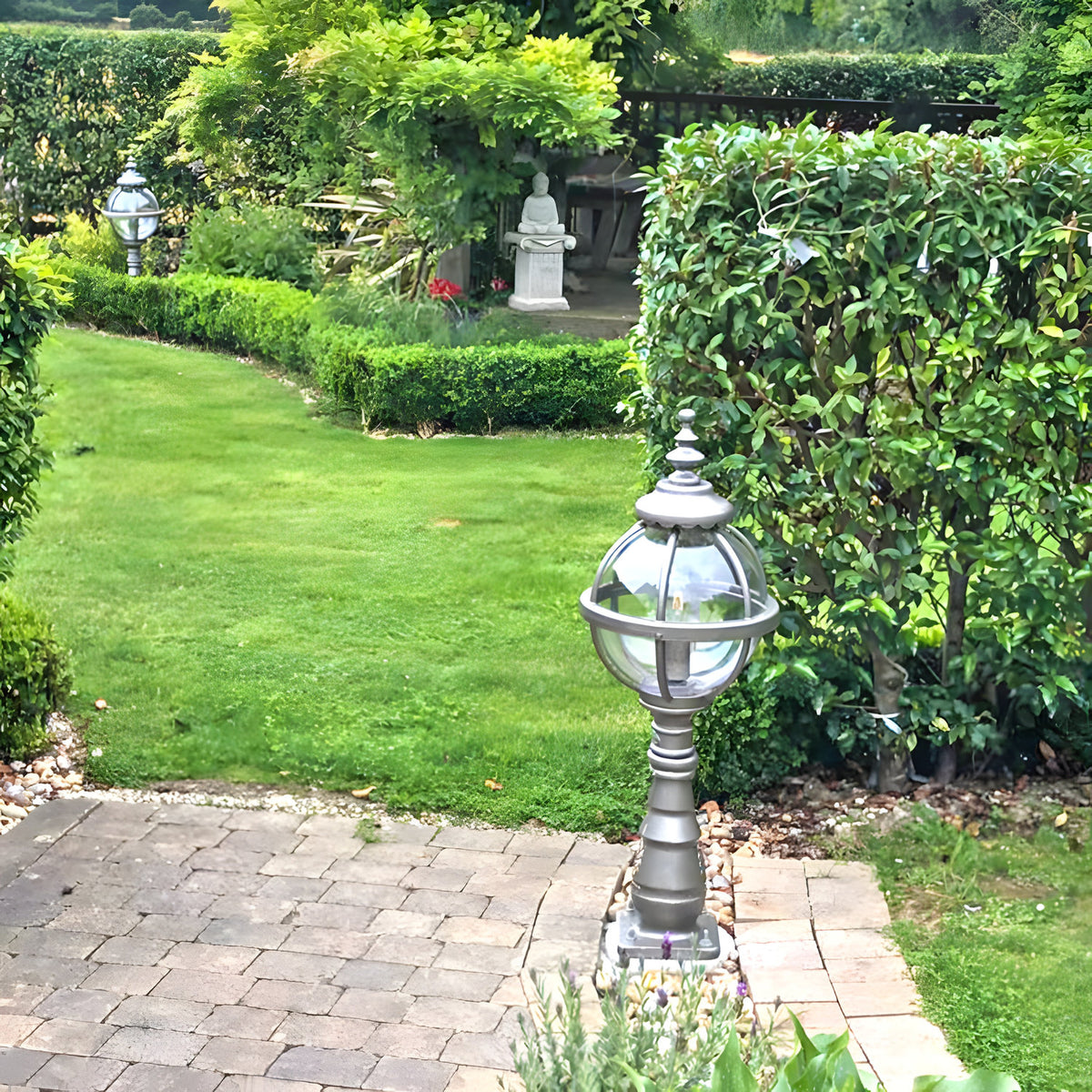 Large Victorian Cast Iron Globe Pedestal Post Light in black, banded cage design on a paved garden path beside a lawn and hedges.
