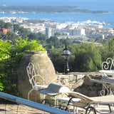 Small Victorian cast iron globe pedestal post light in black on a stone terrace wall, overlooking a coastal town and sea view.
