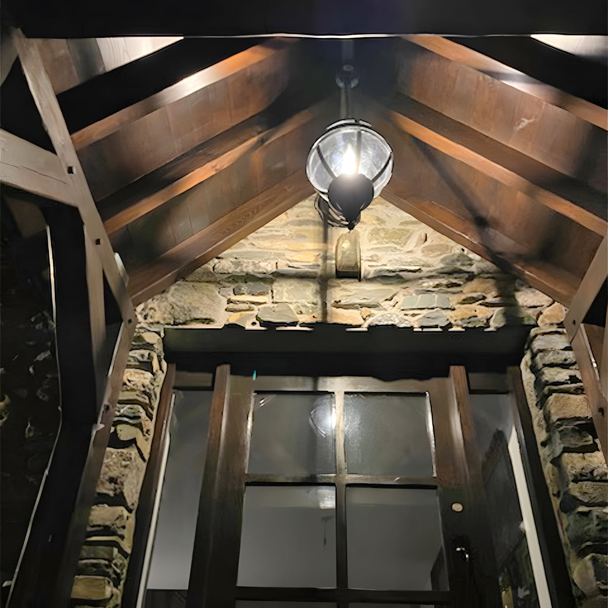 Large Victorian Globe Hanging Lantern on a chain in black, cast iron banded cage over an entrance porch with wood beams and stone walls.